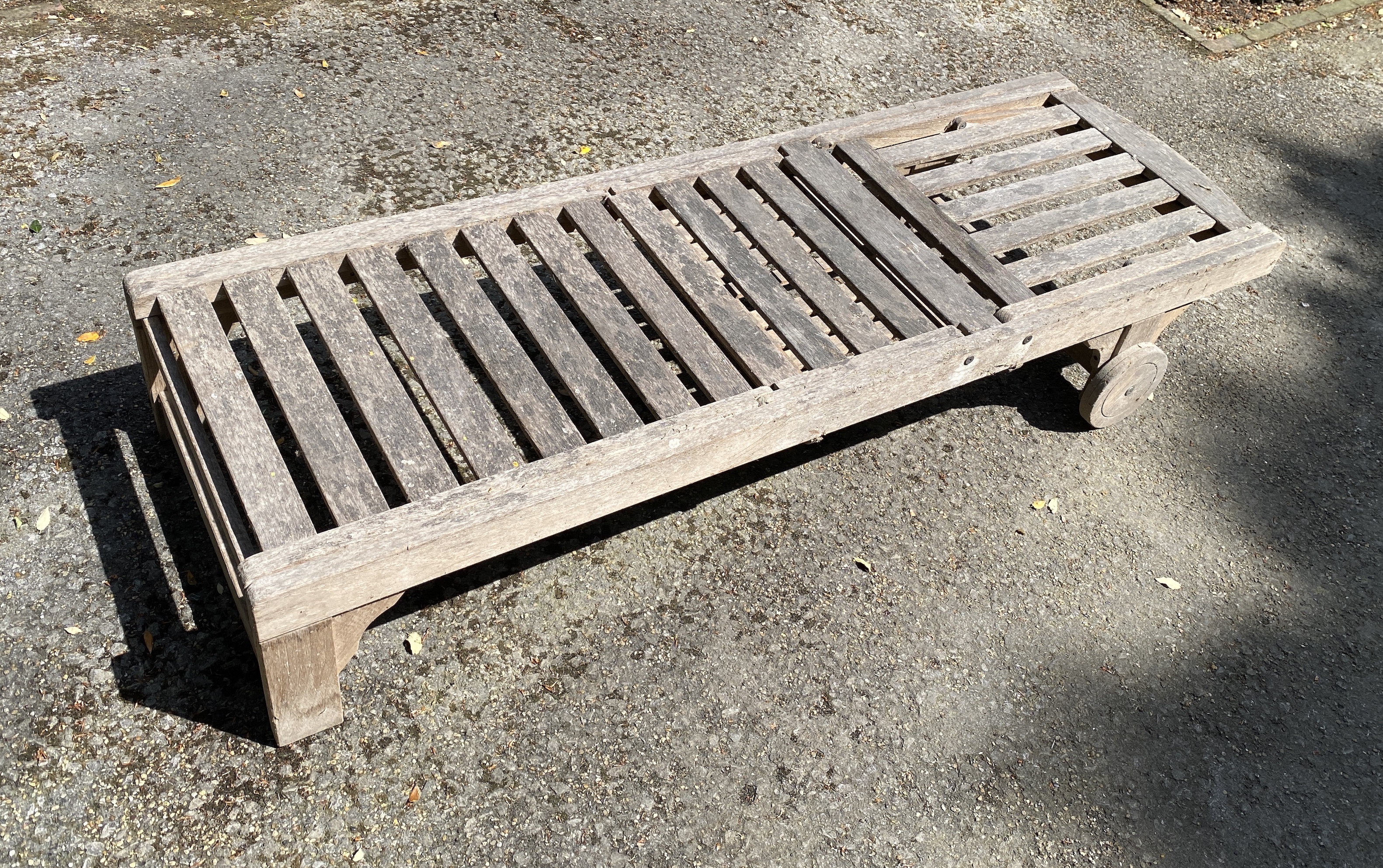 Four slatted teak sun beds, with adjustable backs and integral sliding tables, on two wheels